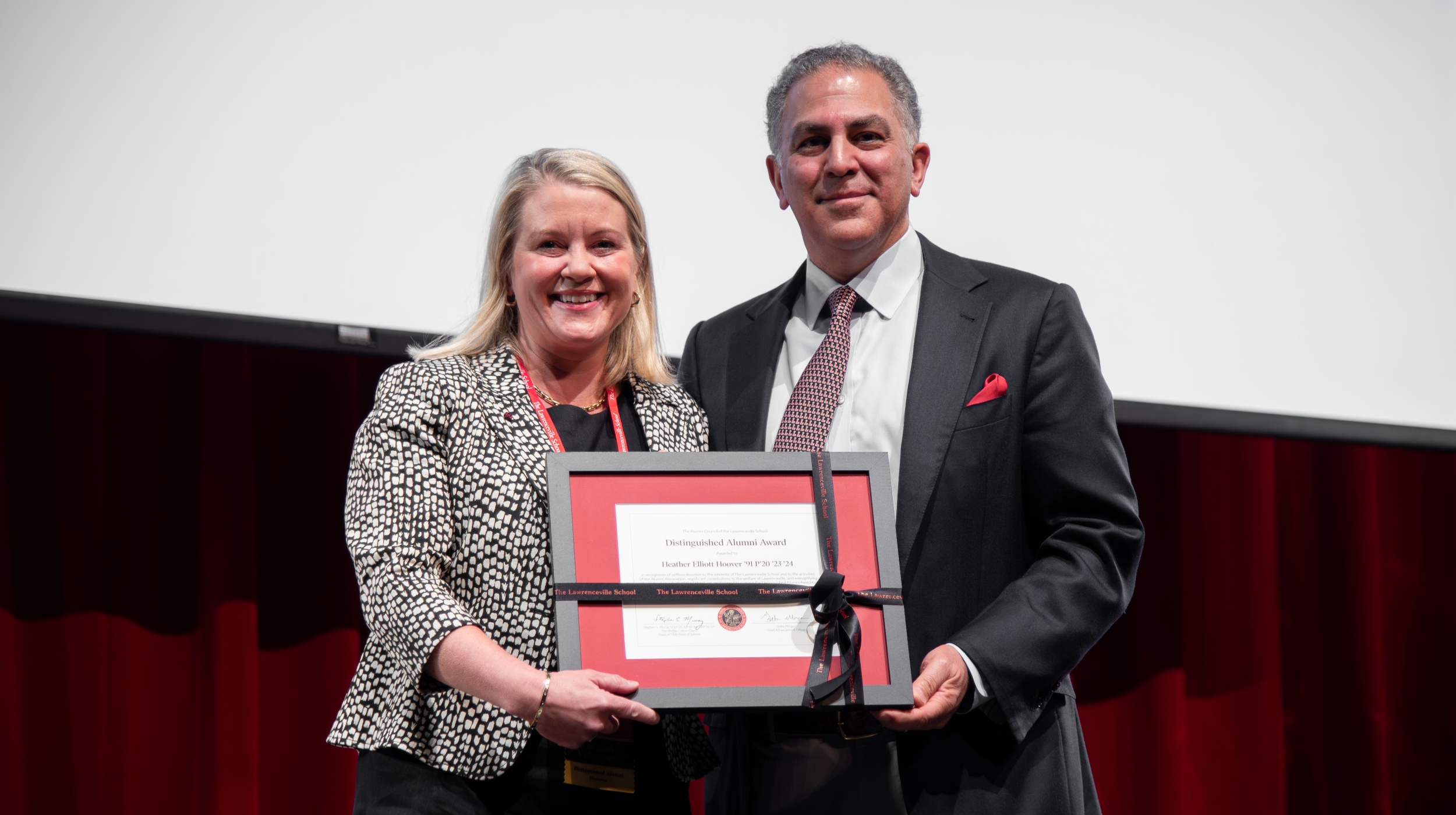 Together, a woman and a man hold a framed certificate wrapped in a black ribbon.
